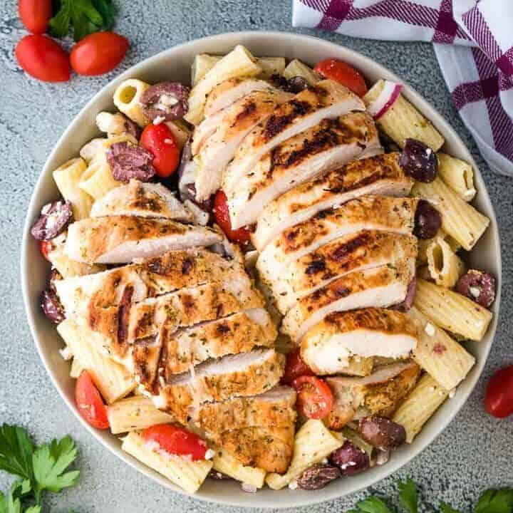Arial view of sliced grilled chicken over greek pasta salad.