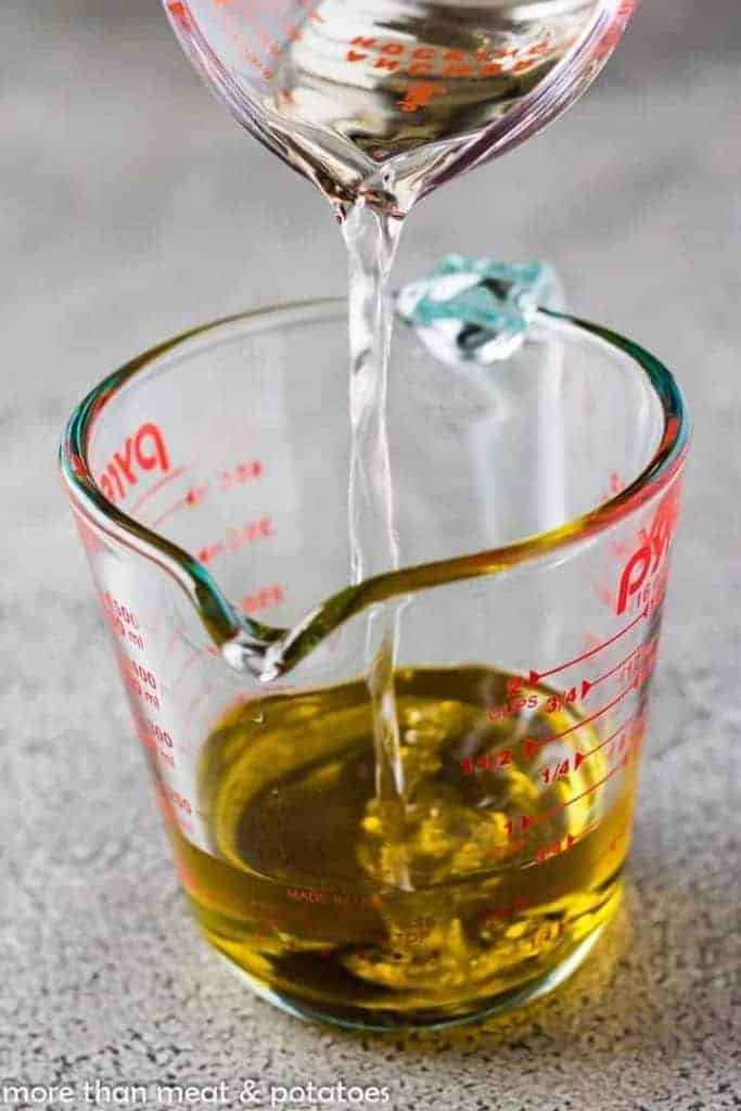 Pouring white wine vinegar into a measuring cup with olive oil.