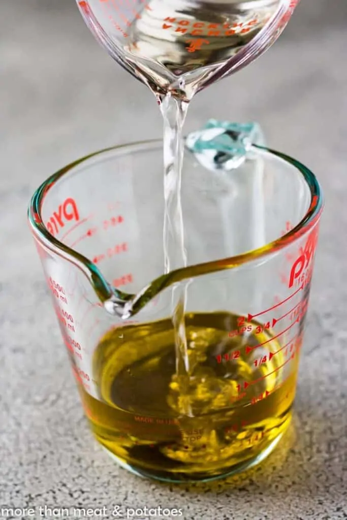 Pouring white wine vinegar into a measuring cup with olive oil.