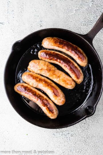 Five Italian sausage links cooking in a skillet.