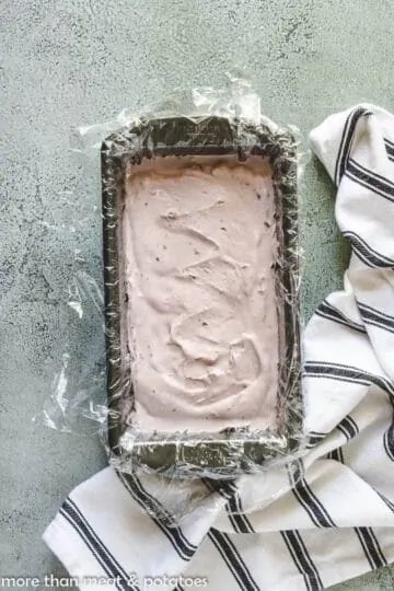 The ice cream in a loaf pan covered with plastic wrap.