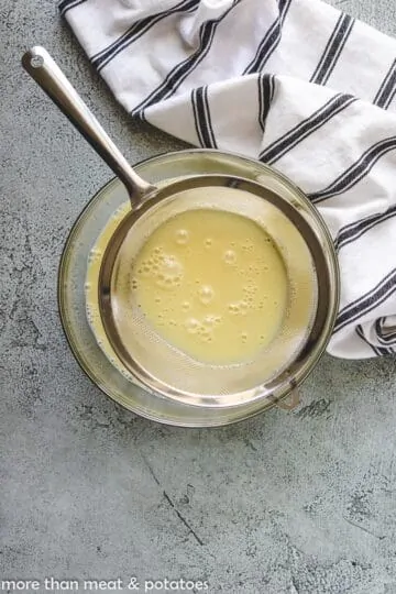 Vanilla custard poured in a bowl through a mesh sieve.