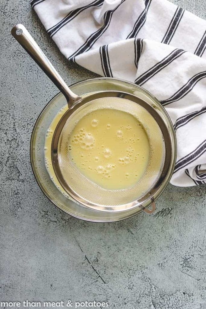 Vanilla custard poured in a bowl through a mesh sieve.