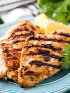 Perfectly grilled chicken on a blue plate with lemon slices.