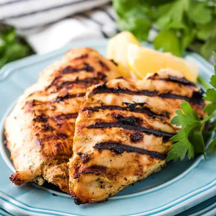 Perfectly grilled chicken on a blue plate with lemon slices.