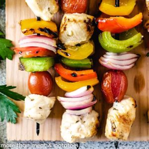 Three skewers with grilled chicken and vegetables on a cutting board.