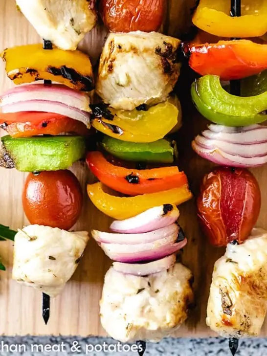 Three skewers with grilled chicken and vegetables on a cutting board.
