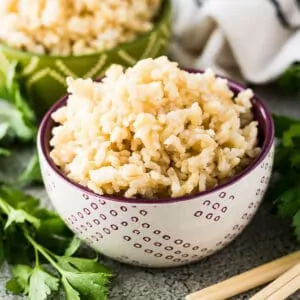 Bowl of brown rice next to fresh parsley and chop sticks.