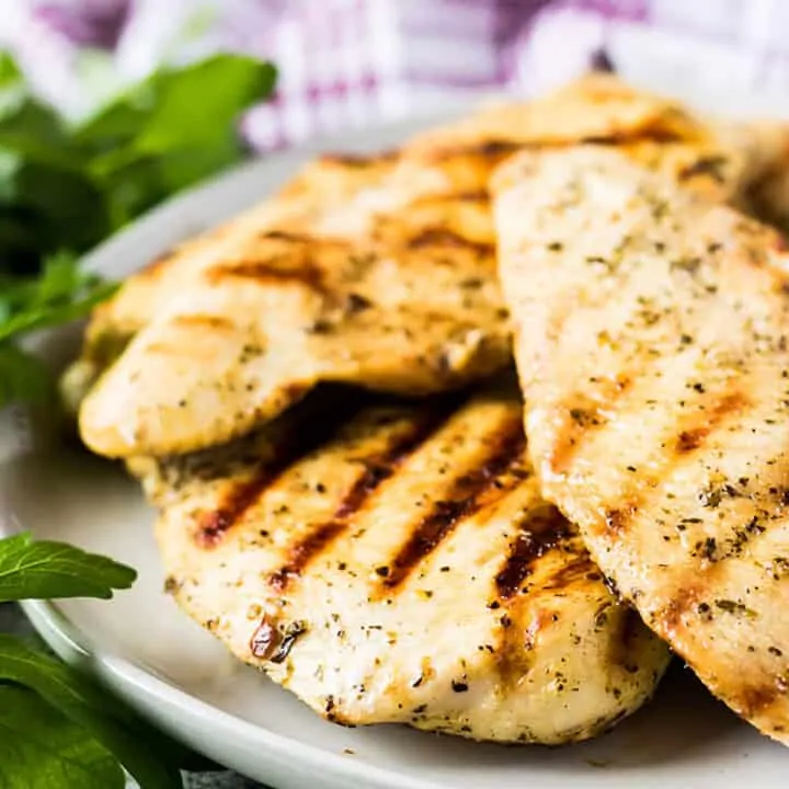 Several grilled chicken breasts on a gray plate next to a purple towel.