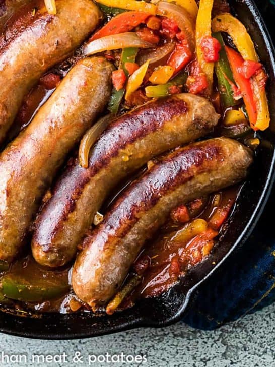 Top down image of Italian sausages and bell peppers in a cast iron pan.