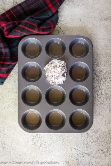 The garlic bulb wrapped in foil in a cupcake pan.