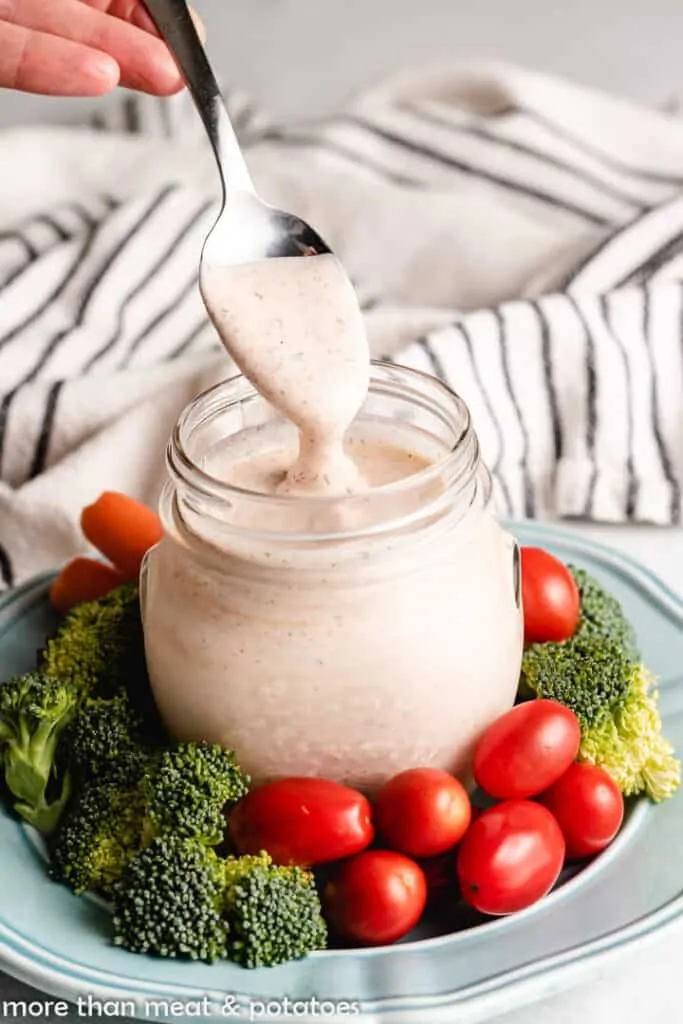 A hand dipping a spoonful of the dressing from the jar.