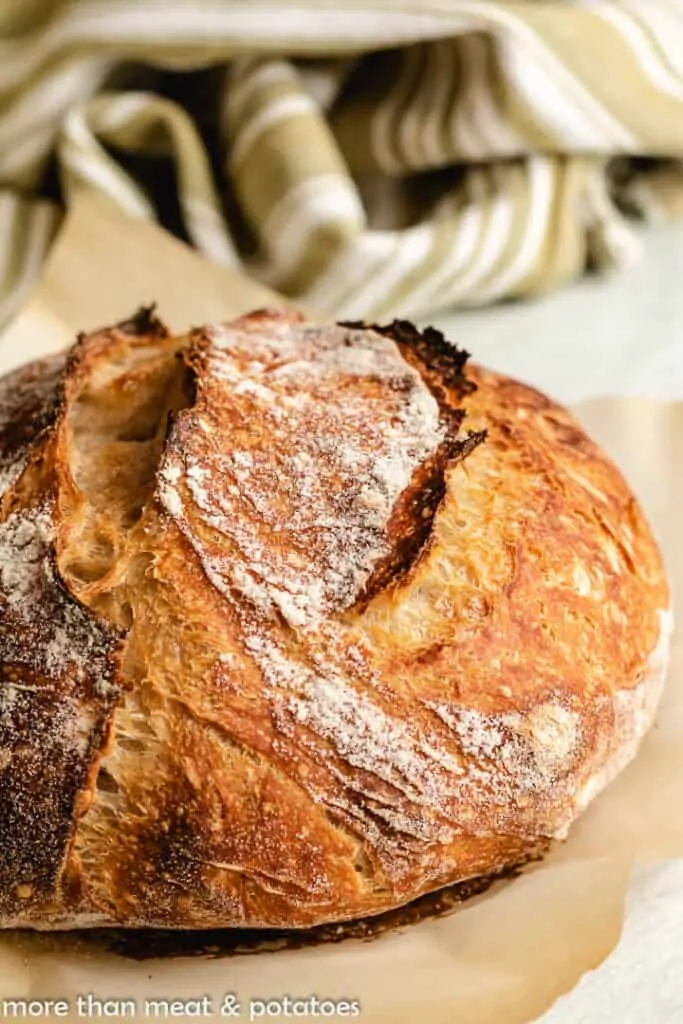 Loaf of baked sourdough on parchment paper with a green towel.