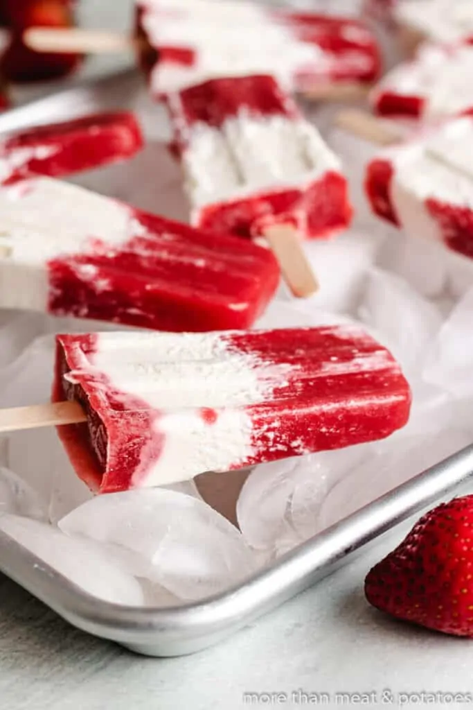 Strawberry cream popsicles on a pan of ice.