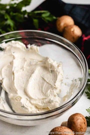 Softened cream cheese in a mixing bowl with herbs.