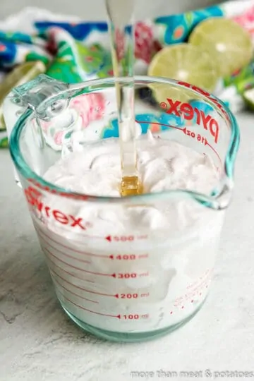 Honey being poured into coconut milk in a measuring cup.