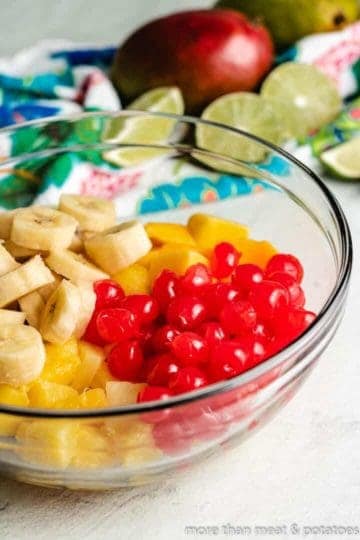 Cherries and sliced bananas and pineapples, in a mixing bowl.