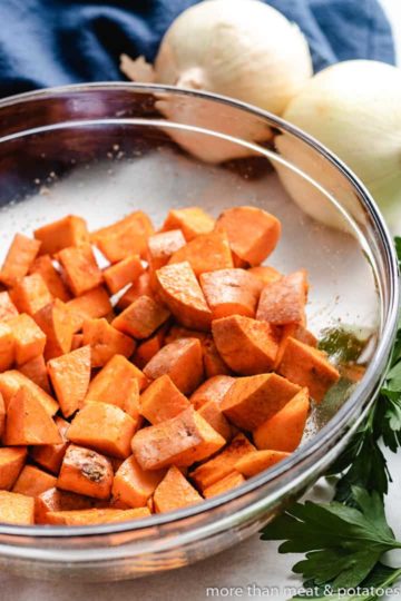 Diced sweet potatoes tossed with avocado oil in a bowl.