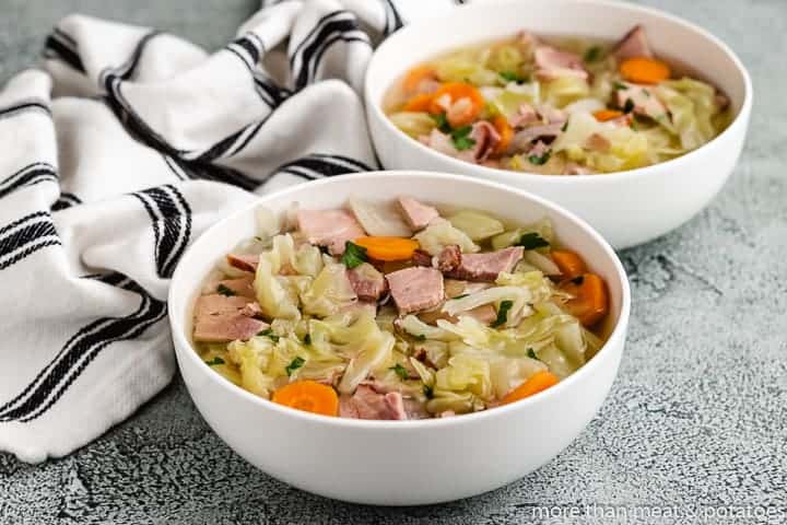 Two white bowls filled with ham and cabbage soup.