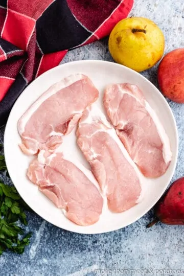 Four raw pork chops on a plate.