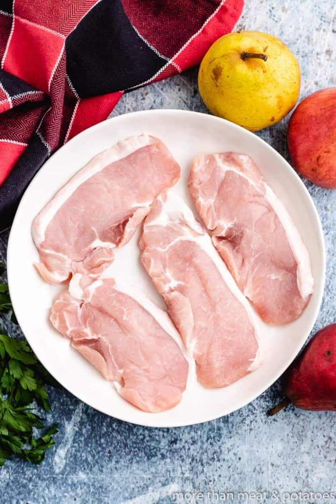 Four raw pork chops on a plate.