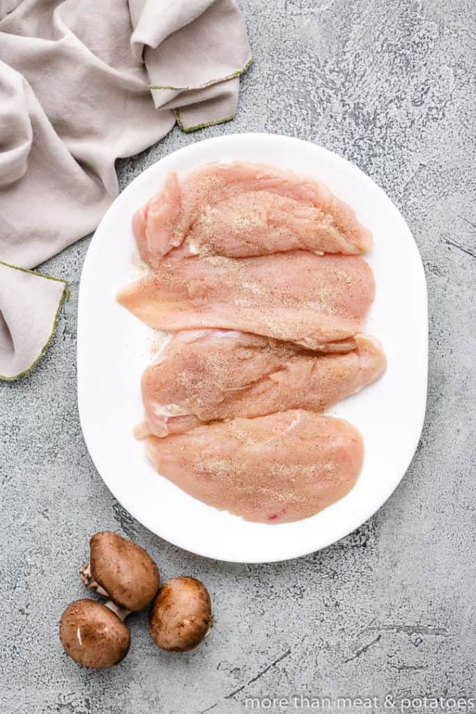 Four raw, seasoned chicken breasts on a platter.