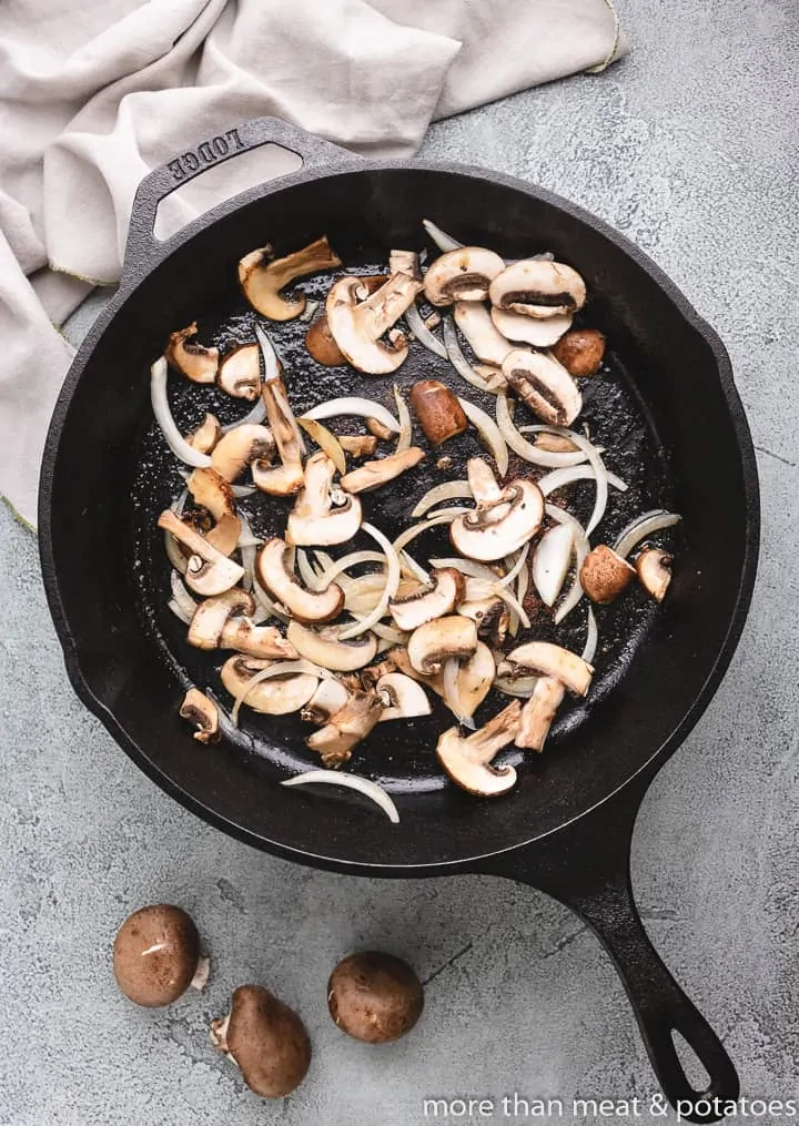 Mushrooms and onions sauteing in a skillet.