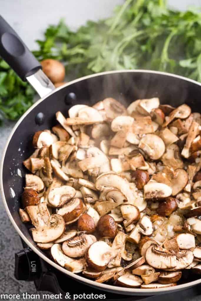 Sliced mushrooms and onions cooking in a saucepan.