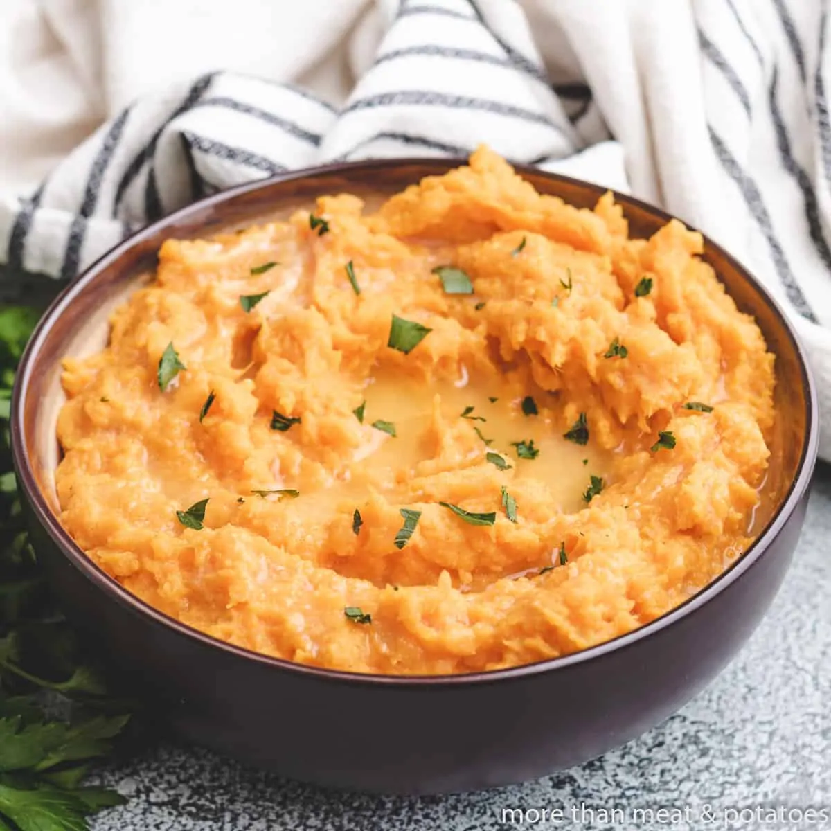 Mashed sweet potatoes in a bowl garnished with parsley.