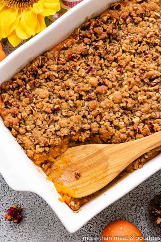 Sweet Potato Casserole with Pecan Streusel The sweet potato casserole with pecans a wooden spoon.