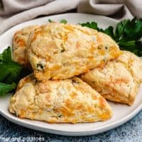 Four cheddar chive scones stacked on a plate.