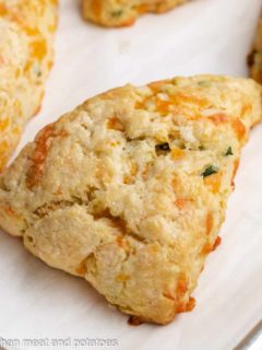A cheddar chive scone sitting on a lined sheet pan.