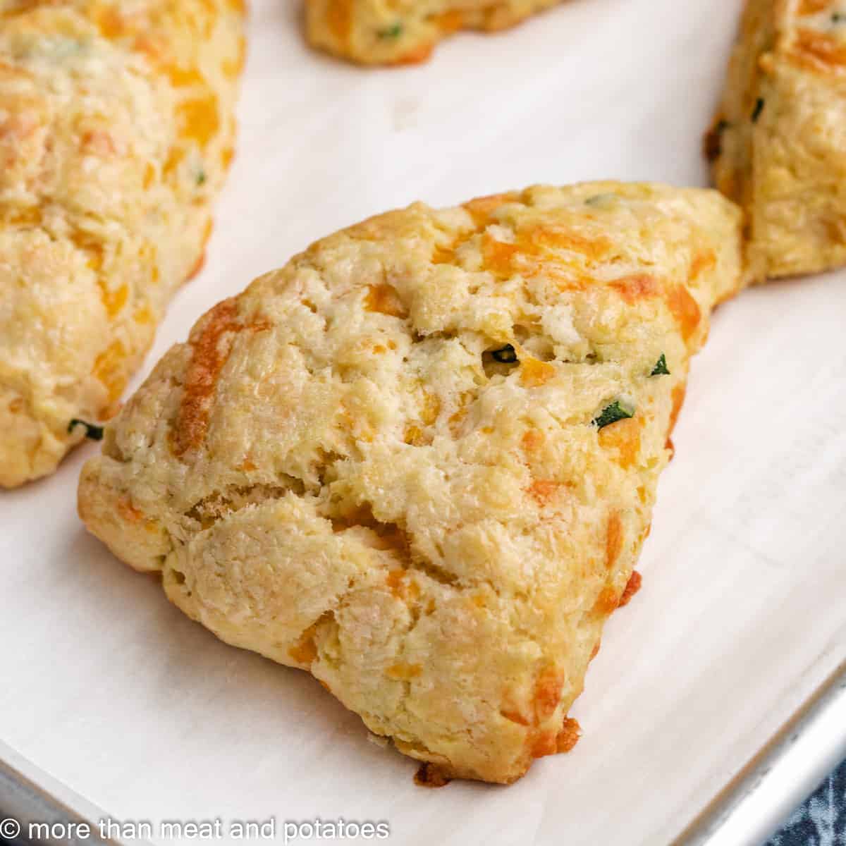 A cheddar chive scone sitting on a lined sheet pan.