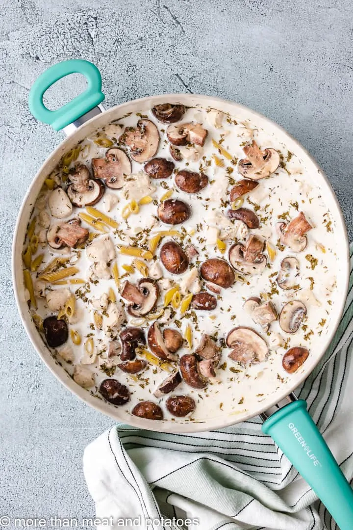 Heavy cream, broth, and dry pasta added to the skillet.