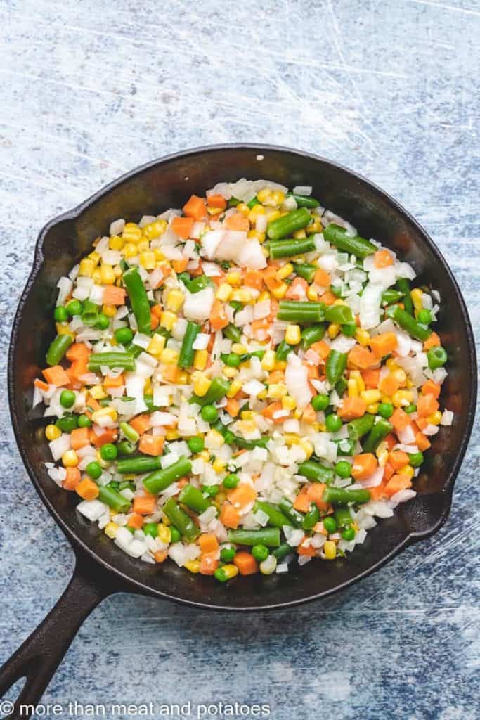 Mixed vegetables cooking in a cast iron skillet.