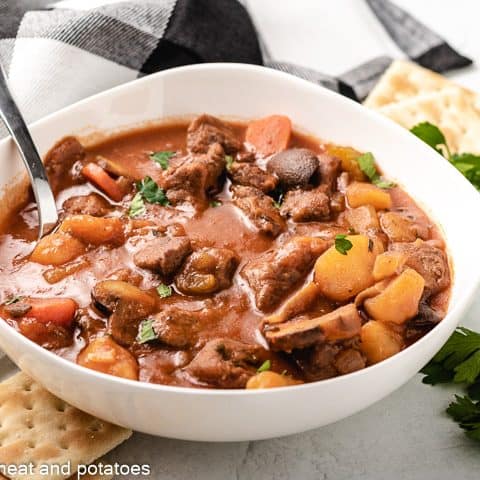 Cooked beef stew with tomato sauce in a white bowl.