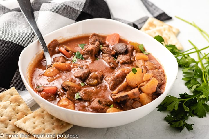 Cooked beef stew with tomato sauce in a white bowl.