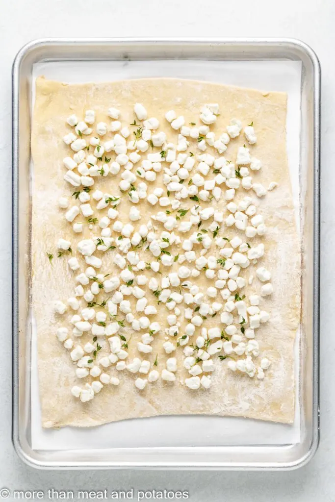 Seasoned goat cheese sprinkled over raw puff pastry dough.