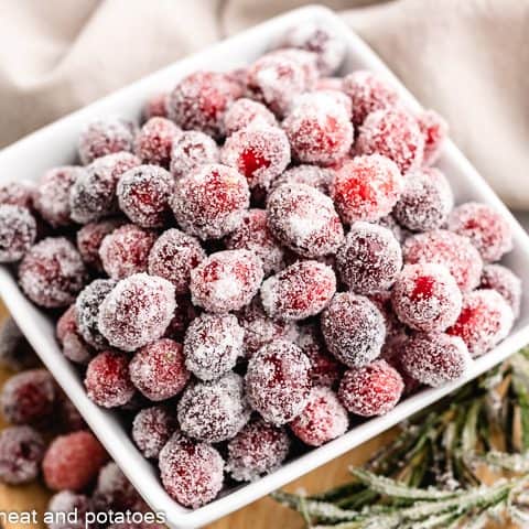 The sugared cranberries with rosemary in a square bowl.