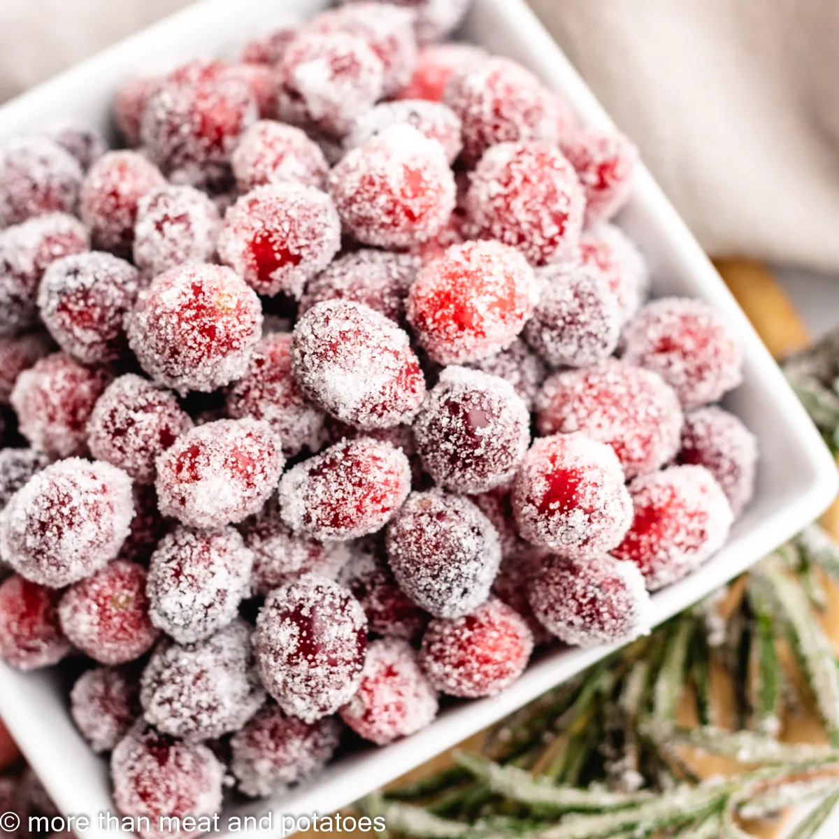 An aerial view of the sugared cranberries with rosemary in a bowl.