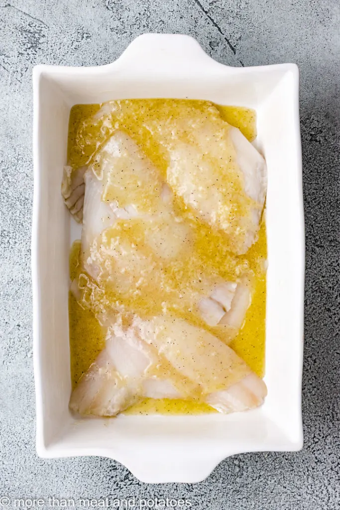 Top down view of flounder with lemon butter in a baking dish.