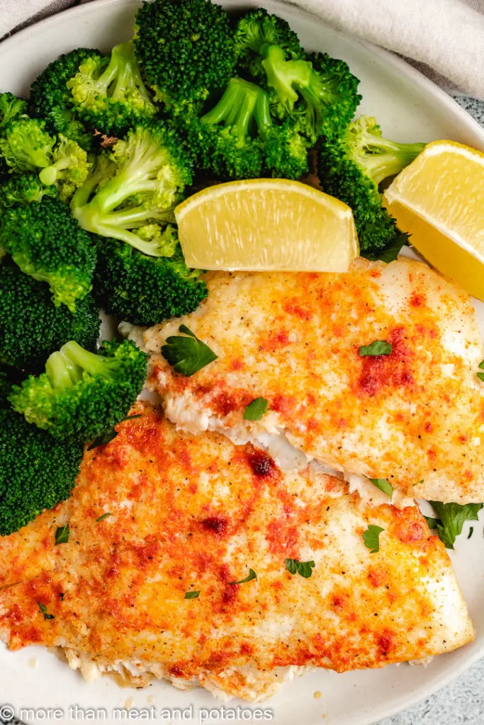Fish fillets with lemon wedges and broccoli florets.