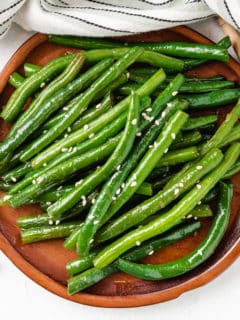 Top down view of Honey Garlic Green Beans on a wooden plate.