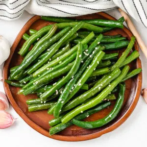 Top down view of honey garlic green beans on a wooden plate.