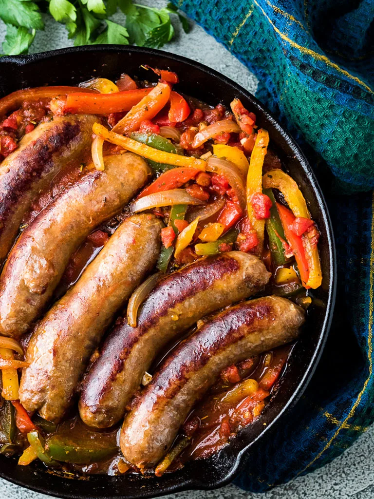 Top down image of italian sausage and peppers in a cast iron skillet.