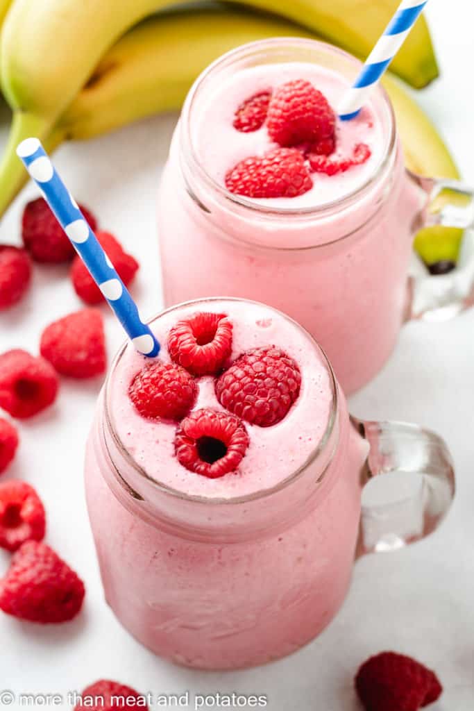 Two raspberry smoothies with straws in mugs.