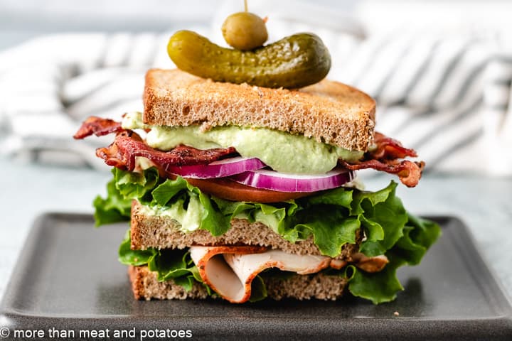 Turkey avocado club on a black plate.