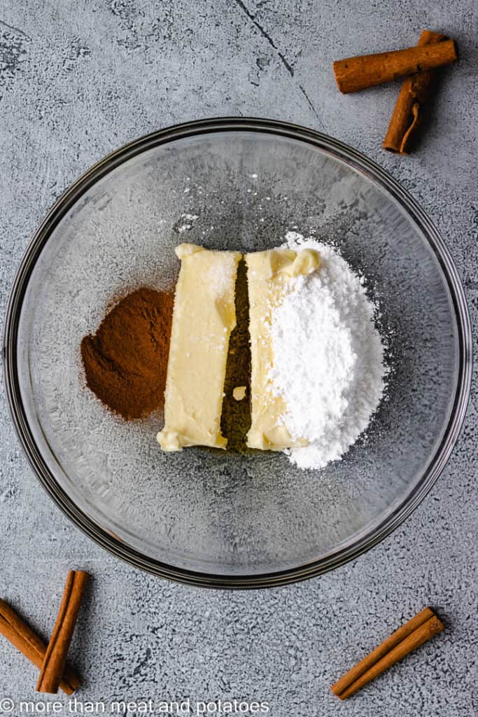 Top down view of butter, powdered sugar, vanilla, and cinnamon in a bowl.