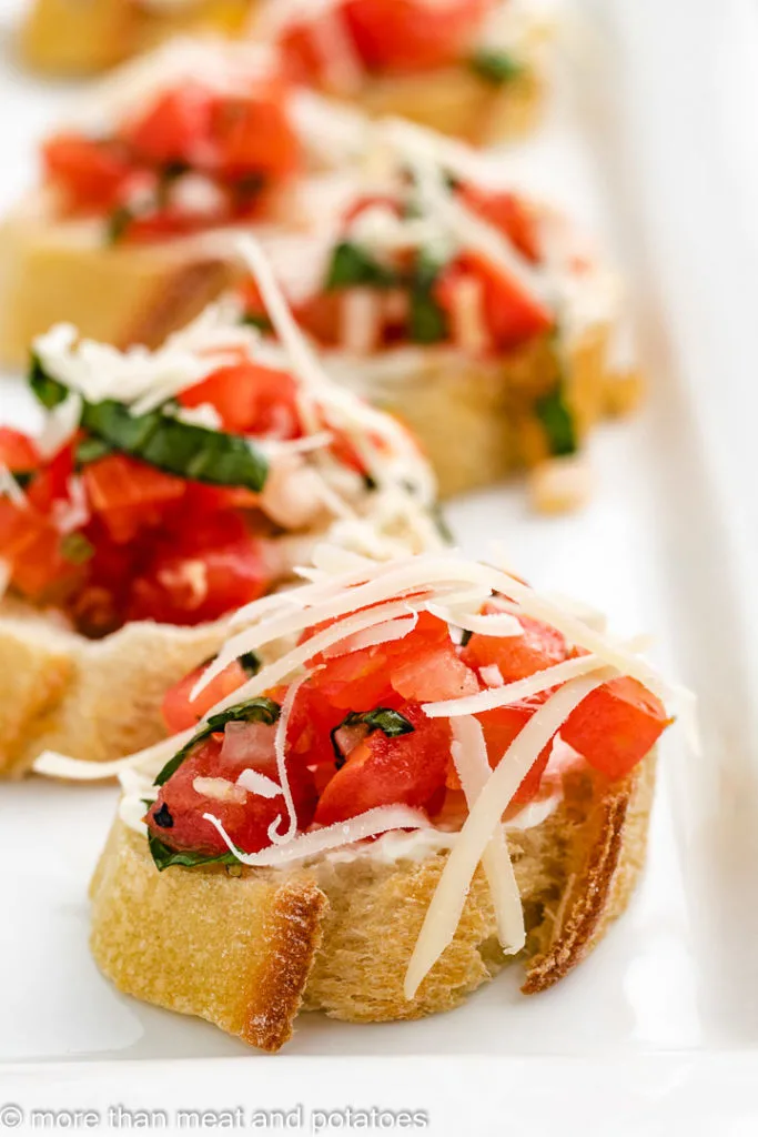 Pieces of tomato bruschetta topped with Parmesan cheese.