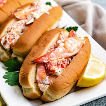 Lobster rolls on a platter with lemon wedges.